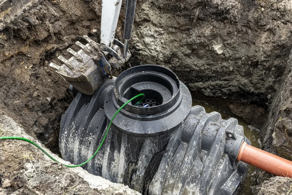 Cuve d’assainissement individuel descendue par une pelle dans sa fouille, raccordée à une canalisation orange