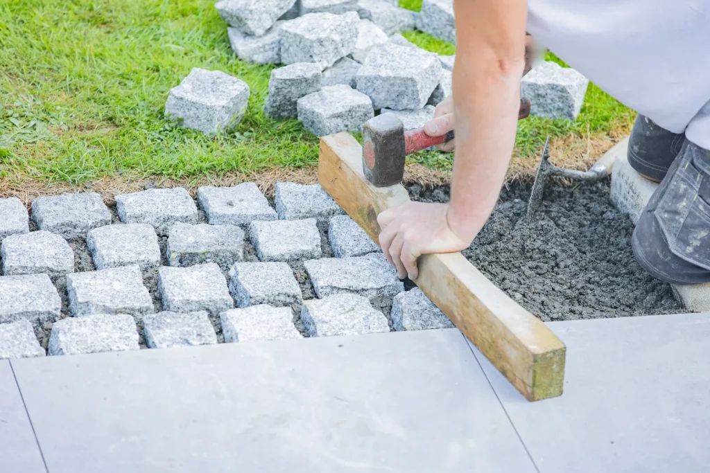 Pose de pavés de granit au maillet, guidée par une règle en bois