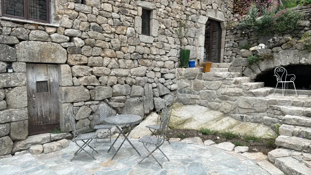 Terrasse dallée et escalier en pierre devant une maison en moellons